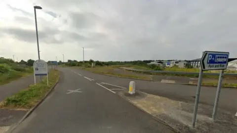 An image of a turning into a road. A sign on a traffic island is directing people to a park and ride. 