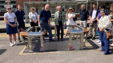 BBC/Naj Modak People surround the steel grid that was installed over the River Sheaf at Sheffield Station. There are perch seats surrounding the installation used to attach engraved information about the history of the river.