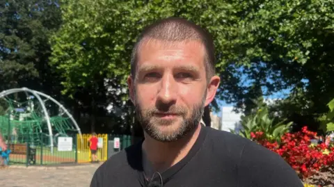 Lee Carpenter is pictured in Jersey's parade gardens, he is wearing a black tshirt and is sat on a bench.