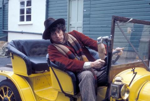 Tom Baker as the 4th Doctor, sitting in Bessie, the yellow roadster car