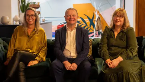 Plaster Communications Three people, a man and two women, smile at the camera as they sit on the sofa. They are all representatives of Bristol Business Improvement Districts, known as BIDS. The man is in the centre of the picture