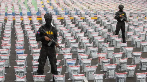 Police officers standing with guns in front of bags of cocaine