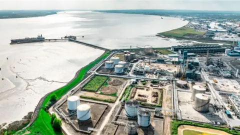 An aerial view of Immingham port. There are large storage tanks on the industrial site. A jetty sticks out from the shore into the river.