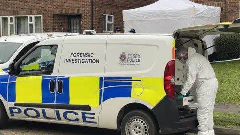 Stephen Huntley/BBC A police forensics van parked up in a residential road. The boot is open and a person in a white full-body forensics overall is leaning into the back of the open van.