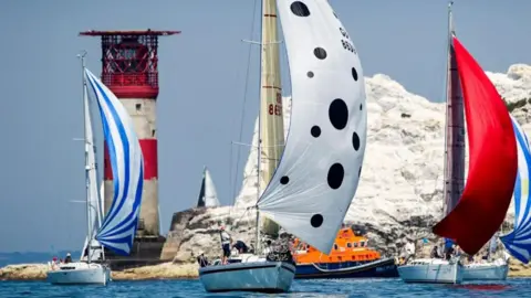 Sailing boats at The Needles, with colourful spinnakers and The Needles lighthouse behind.