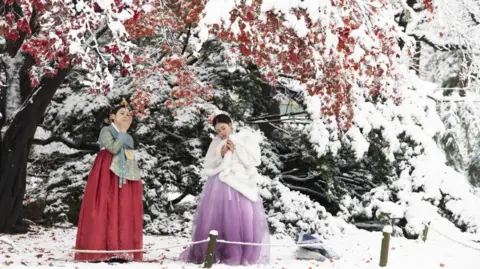 EPA-EFE/REX/Shutterstock Macao tourists wearing Korean traditional Hanbok dresses take pictures amid snowfall at the Gyeongbokgung Palace in Seoul, South Korea, 27 November 2024.