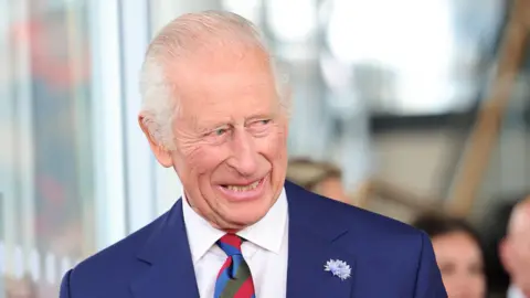 PA Media A smiling King Charles looking to the right of the camera, dressed in a suit and multi-coloured tie.