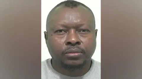 Mugshot of Ahmed. He has a short black goatee beard and shaved head with short black hair on top.