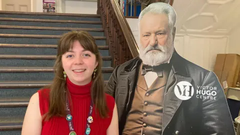 A woman with brown hair smiling, she has blue eyes and is wearing a red top.