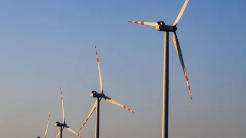 Four wind turbines in a row against blue-red sky