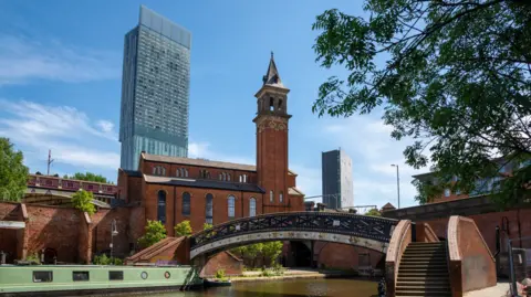 Getty Images A shot of Manchester with a canal, bridge and boat in the foreground and the Beetham Tower in the background