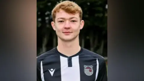 Family A male teenager with short ginger hair is wearing a black and white football shirt and smiling.