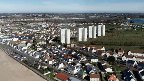 BBC An aerial view of housing by a beach and with housing blocks of flats.