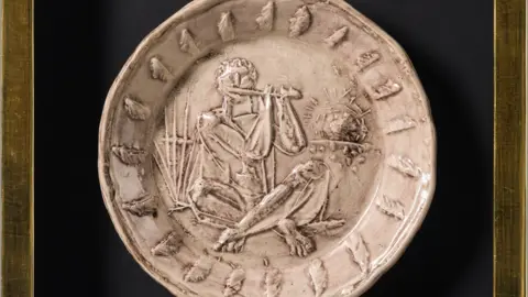 Castle Fine Art Ceramic white dish with a pattern of a man sitting cross-legged while playing the flute.