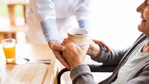 Getty Images Social carer helps a lady have a drink 