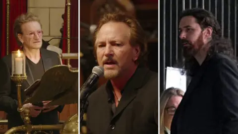 A composite image of three men. On the left, a man with medium length brown and blond hair stands behind a candle. Behind him are red curtains. He is wearing a pair of pink glasses, a brown top, and a dark suit jacket. In the middle, a man with medium length brown hair stands at a microphone. He has a beard and is wearing a dark top. On the right, there is a man with long dark hair and a beard. He is wearing dark clothing. 