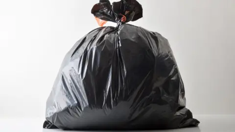A black bin bag tied at the top and photographed against a white background.