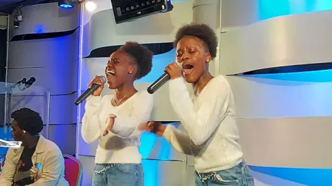 Twins Shanice and Andrea Nyandoro singing on a small stage and their local church