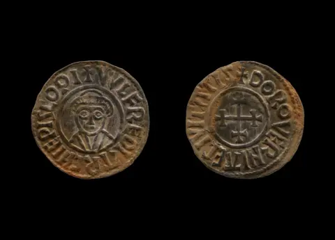 A silver ingot coin which has shows a man on one side and a cross on the other
