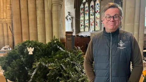 A bespectacled Father Stuart Cradduck standing in front of the toppled tree.