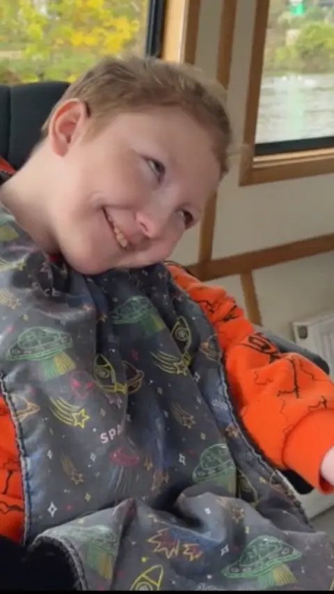 Child smiling with an orange jumper and a space-themed blanket on top.