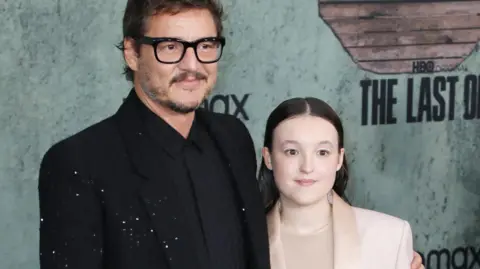 EPA On the left is a man with short dark hair and stubble. He has black glasses and is wearing a black shirt and black jacket. To the right is a young woman, in a light pink jacket and light-coloured shirt. She has shoulder-length dark hair. They are posing at the premiere of the TV show The Last of Us, and are standing in front of a background that features the logo for the show and that of streaming service HBO Max. 