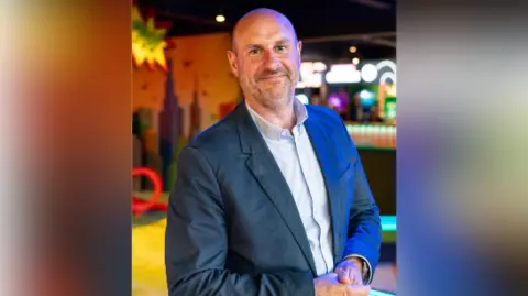 Adventure Leisure Bald man stands in a suit smiling posing for picture.