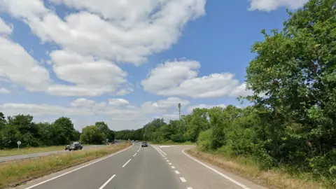 Google Street view image of the A33 dual carriageway at the Barge Lane junction. The view is facing the oncoming traffic on the southbound carriageway. There is a junction with a small slip road for drivers leaving and joining at Barge Lane. The wide two-lane dual carriageway is lined with dense green trees and hedgerows.