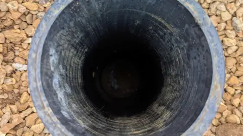 RSPCA A pipe is in a gravel drive. There appears to be something in it but the image is dark and unclear