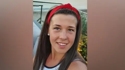 Family handout Jennifer Poole. She has long dark brown hair, has a nose ring, and wearing a red headband, pearl earrings and white vest top.