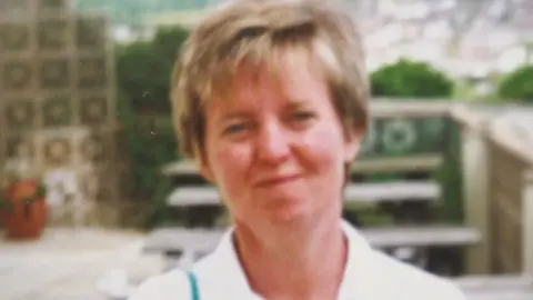 Supplied Softly blurred portrait of a Judith with short hair, pictured outside in a garden setting with a stone wall, greenery and seating in the background.
