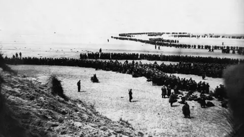 Getty Images Thousands of soldiers line a beach in a black and white photo