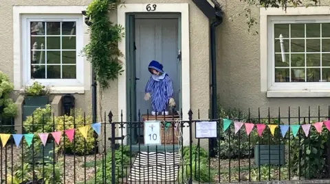 Andy Pandy scarecrow in a doorway, with a traditional cast iron gate and bunting.