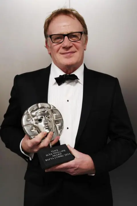 Getty Images A man with brown hair and glasses, wearing a tuxedo and holding a Bafta Cymru award.