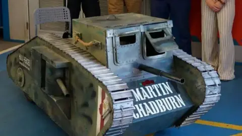 Hull 4 Heroes A homemade kart in the shape of a military tank. It reads "MARTIN CHADBURN" on the front in white capital letters. It is parked inside on a blue carpet. 
