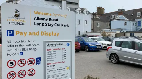 A car park sign to the left with cars parked to the right of it