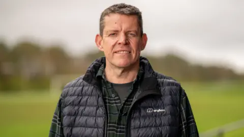 Rhun ap Iorwerth in a black gilet and chequered shirt