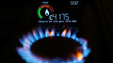 PA Media A gas ring on a stove lit with blue and orange flames with the reading of a smart metre above it.