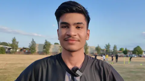 Mohammad has short dark hair quiffed over, and is wearing a black t-shirt.