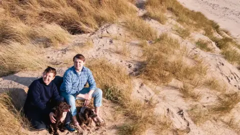 Will Matthews and his brother Jack sit on a sand dune with their dog