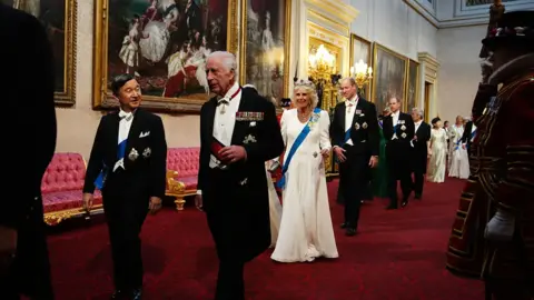 PA The Emperor and King walking together in Buckingham Palace, followed by the Queen, Empress, Prince William and other Royals. Beefeaters stand at the side