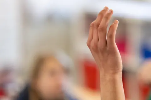 Getty Images Anonymous photo of child holding up their hand in classroom