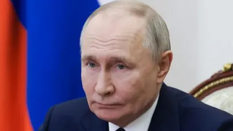 Reuters Head and shoulders picture of Vladimir Putin, wearing a dark suit and matching tie, with a Russian flag behind him.