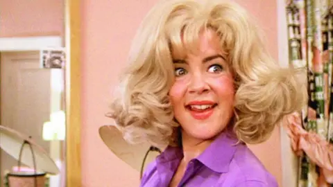 Getty Images A smiling woman in a blonde wig wearing a purple shirt
