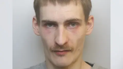 Avon and Somerset Police A custody picture of Daniel Gunter, who has dark blonde hair and a blonde moustache. He is looking at the camera with a serious expression, and has dark red patches under his eyes. 