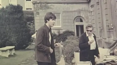 Sir Paul McCartney is in the middle of the photo outside a building, with another man on the right.