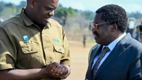 Energy Minister Deogratius Ndejembi (L) in greenish brown shirt speaks to Vice-President Emmanuel Nchimbi (R) 