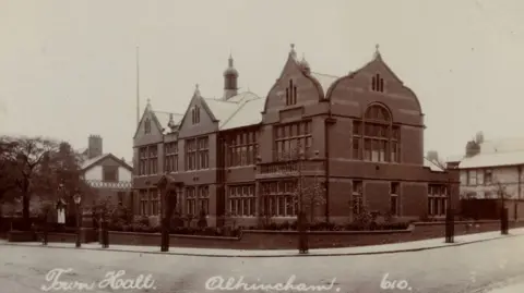Trafford Council A black-and-white period photograqh of Altrincham Town Hall from Trafford Council's archive. The brick building stands on the corner of a road. 