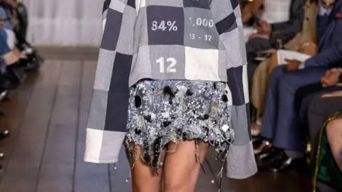 Chris Yates A model walking the runway wearing grey sweatshirt and silver embellished skirt.