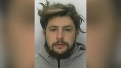 South West ROCU Mugshot of a man with messy short brown hair and facial hair. He is wearing a grey zip-up hoodie